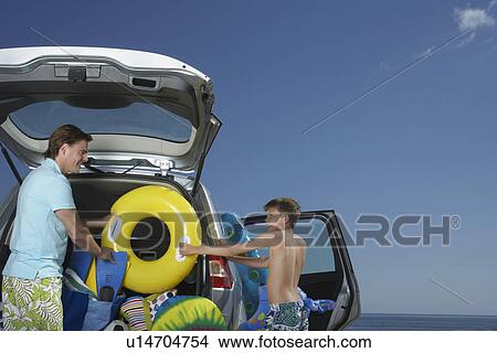 Father and son (10-12) unloading car full of beach accessories View Large Photo Image Picture - Father and son (10-12) unloading car full of beach accessories. Fotosearch