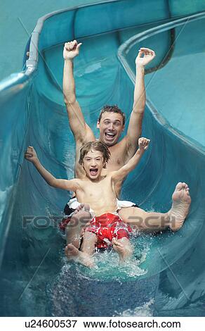 Stock Photo - Father and son (7-9) with arms outstretched on water slide. Fotosearch