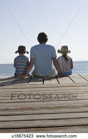 Father and two children (7-9) sitting on jetty back view View Large Photo Image Stock Image - Father and two children (7-9) sitting on jetty back view. Fotosearch