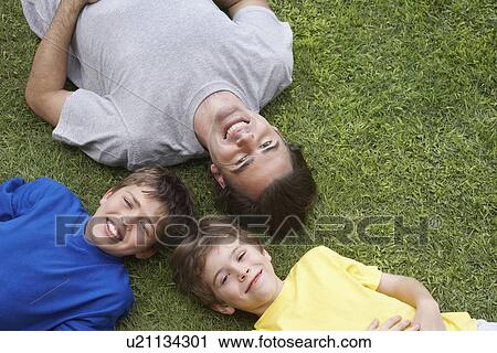 Stock Image - Father and two sons (6-11) lying on grass view from above. Fotosearch