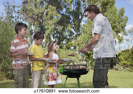 Stock Image - Father serving grilled food to children (5-11) in line. Fotosearch