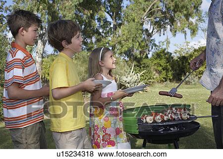 Father serving grilled food to children (5-11) in line close-up View Large Photo Image Stock Photo - Father serving grilled food to children (5-11) in line close-up. Fotosearch