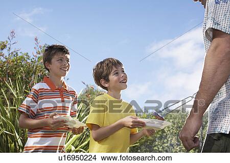 Picture - Father serving grilled frankfurters to sons (6-11). Fotosearch