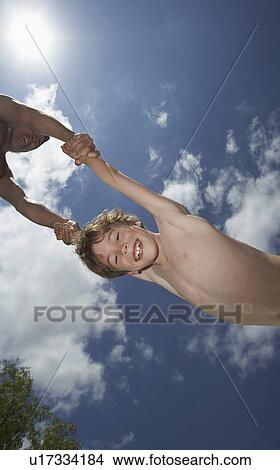 Picture - Father swinging son (10-12) in the air view from below. Fotosearch