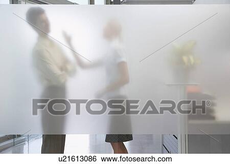 Stock Photograph - Female office worker arguing with male colleague behind translucent wall in office. Fotosearch