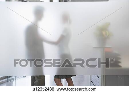 Female office worker touching male colleague behind translucent wall in office View Large Photo Image Stock Photo - Female office worker touching male colleague behind translucent wall in office. Fotosearch