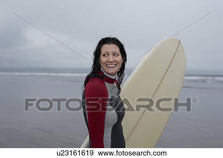 Female surfer carrying surfboard standing in shallow water View Large Photo Image Stock Photo - Female surfer carrying surfboard standing in shallow water. Fotosearch