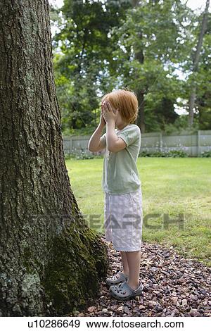 Girl (3-4) standing in front of tree covering eyes View Large Photo Image Stock Photo - Girl (3-4) standing in front of tree covering eyes. Fotosearch