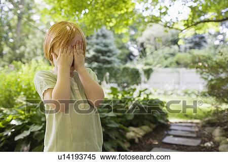 Stock Photography - Girl (3-4) standing in garden covering eyes. Fotosearch
