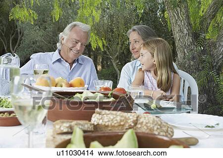 Grandparents with granddaughter (5-6) sitting at garden table View Large Photo Image Picture - Grandparents with granddaughter (5-6) sitting at garden table. Fotosearch