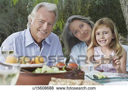 Grandparents with granddaughter (5-6) sitting at garden table portrait View Large Photo Image Stock Photo - Grandparents with granddaughter (5-6) sitting at garden table portrait. Fotosearch
