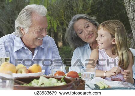 Grandparents with granddaughter (5-6) sitting at garden table View Large Photo Image Stock Photo - Grandparents with granddaughter (5-6) sitting at garden table. Fotosearch
