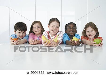 Stock Image - Group of five children (6-9) holding various fruits portrait. Fotosearch