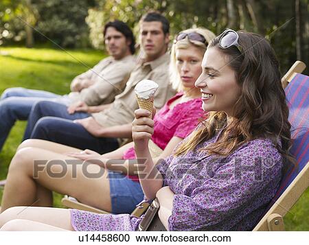 Stock Image - Group of young people sitting in row on deckchairs in garden side view. Fotosearch