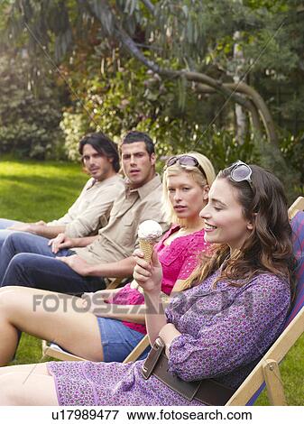 Stock Photo - Group of young people sitting in row on deckchairs in garden side view. Fotosearch