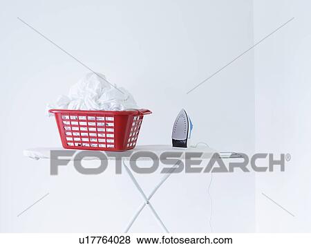 Iron and laundry basket on ironing board against white wall View Large Photo Image Stock Photo - Iron and laundry basket on ironing board against white wall. Fotosearch
