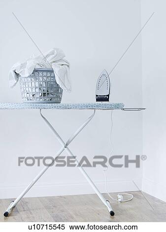 Iron and laundry basket on ironing board against white wall View Large Photo Image Stock Photography - Iron and laundry basket on ironing board against white wall. Fotosearch