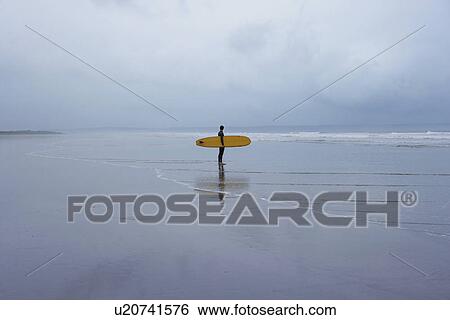 Lone surfer standing in shallow water side view View Large Photo Image Stock Photograph - Lone surfer standing in shallow water side view. Fotosearch