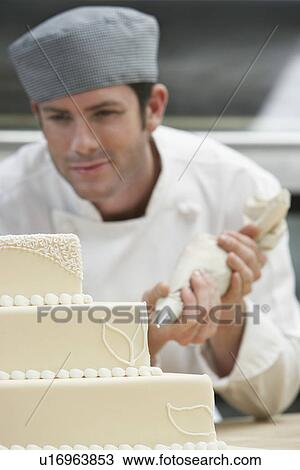 Male chef icing wedding cake in kitchen View Large Photo Image Stock Image - Male chef icing wedding cake in kitchen. Fotosearch