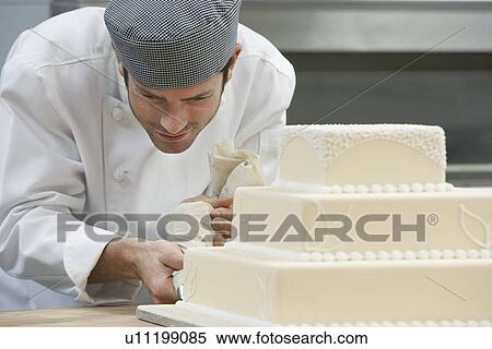 Male chef icing wedding cake in kitchen View Large Photo Image Stock Photography - Male chef icing wedding cake in kitchen. Fotosearch