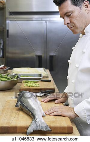 Stock Image - Male chef observing salmon in kitchen. Fotosearch