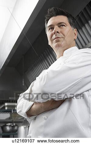 Male chef with arms crossed in kitchen low angle view View Large Photo Image Stock Photo - Male chef with arms crossed in kitchen low angle view. Fotosearch