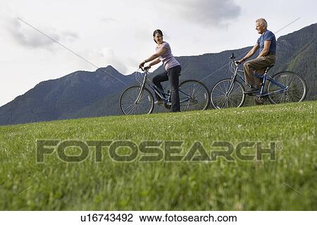 Stock Image - Man and woman biking mountain range in background. Fotosearch