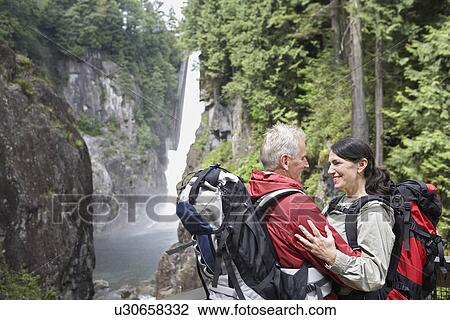 Man and woman embracing carrying backpacks waterfall in background View Large Photo Image Stock Image - Man and woman embracing carrying backpacks waterfall in background. Fotosearch