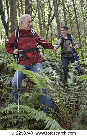 Stock Image - Man and woman in forest carrying backpacks holding hands. Fotosearch