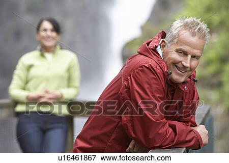Stock Photo - Man and woman in mountains focus on man leaning on railing. Fotosearch