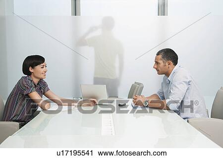 Man and woman talk over conference table man on mobile phone visible through translucent office wall View Large Photo Image Stock Image - Man and woman talk over conference table man on mobile phone visible through translucent office wall. Fotosearch