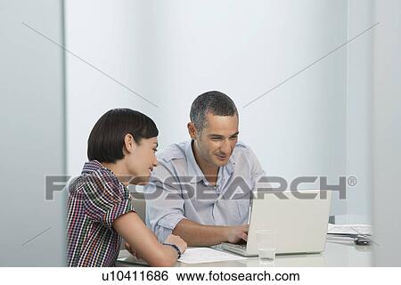 Stock Photograph - Man and woman working at laptop in office smiling. Fotosearch