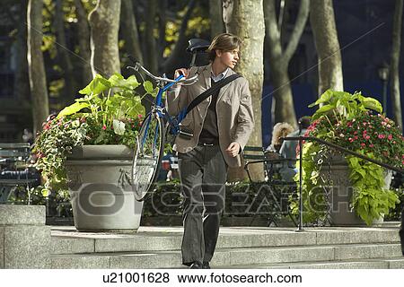 Stock Photo - Man carrying bicycle down steps in park. Fotosearch