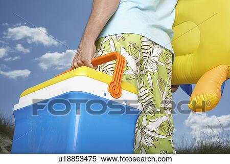 Stock Photography - Man carrying inflatable toy and cool box mid section back view. Fotosearch