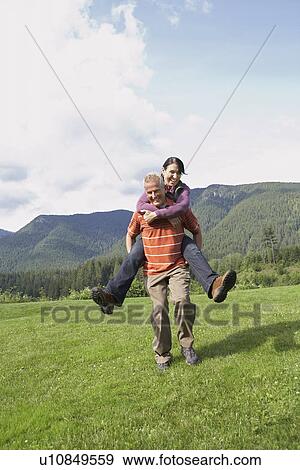 Man carrying woman piggy back in meadow laughing View Large Photo Image Stock Photo - Man carrying woman piggy back in meadow laughing. Fotosearch