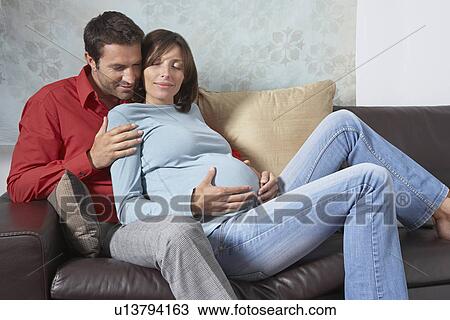 Man embracing pregnant woman on couch in living room View Large Photo Image Stock Image - Man embracing pregnant woman on couch in living room. Fotosearch