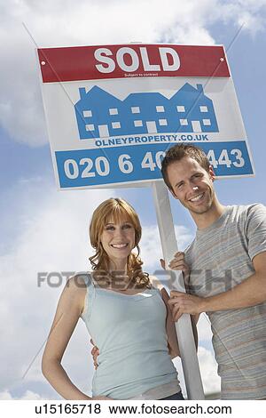 Man embracing woman holding sold sign against sky View Large Photo Image Stock Photo - Man embracing woman holding sold sign against sky. Fotosearch