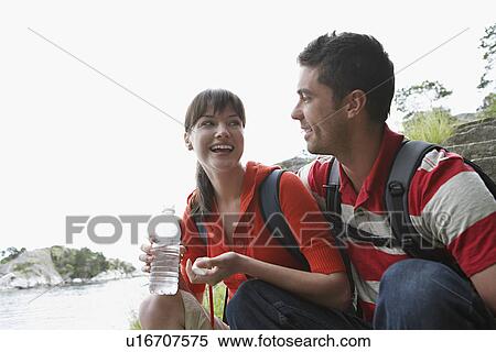 Stock Photography - Man embracing woman holding water bottle near ocean. Fotosearch