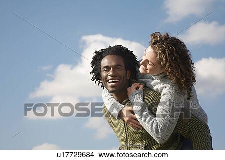 Man giving woman piggyback against sky View Large Photo Image Picture - Man giving woman piggyback against sky. Fotosearch