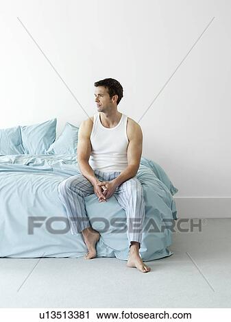 Stock Image - Man in nightwear sitting on bed. Fotosearch