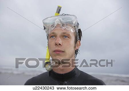 Stock Image - Man in wetsuit wearing snorkle standing on beach portrait. Fotosearch