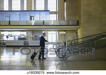 Man looking at watch by escalator in airport lobby View Large Photo Image Stock Photography - Man looking at watch by escalator in airport lobby. Fotosearch