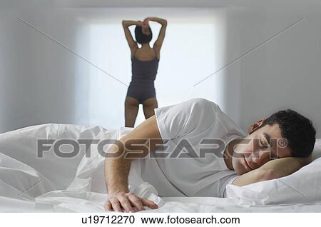 Man lying in bed woman standing by window in background View Large Photo Image Stock Image - Man lying in bed woman standing by window in background. Fotosearch
