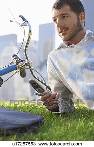 Stock Image - Man lying on lawn in park holding mobile phone close-up. Fotosearch