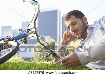 Stock Photo - Man lying on lawn in park looking at mobile phone close-up. Fotosearch