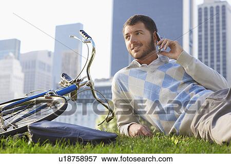Stock Photo - Man lying on lawn in park talking on mobile phone. Fotosearch