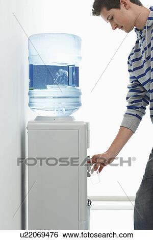 Stock Photograph - Man pouring drink from water cooler indoors. Fotosearch