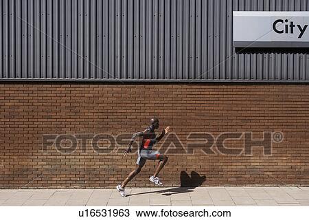 Stock Image - Man running past brick wall with 'city' written on it. Fotosearch