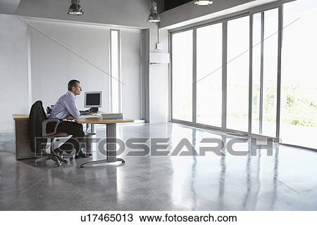 Stock Image - Man sitting at desk in empty office building. Fotosearch