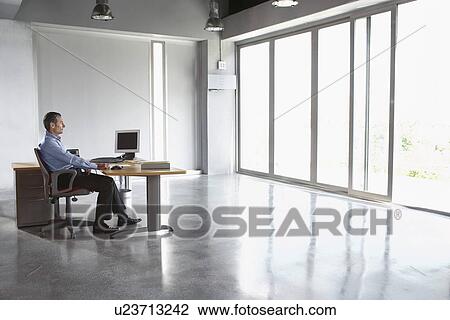 Man sitting at desk in empty office building View Large Photo Image Stock Image - Man sitting at desk in empty office building. Fotosearch